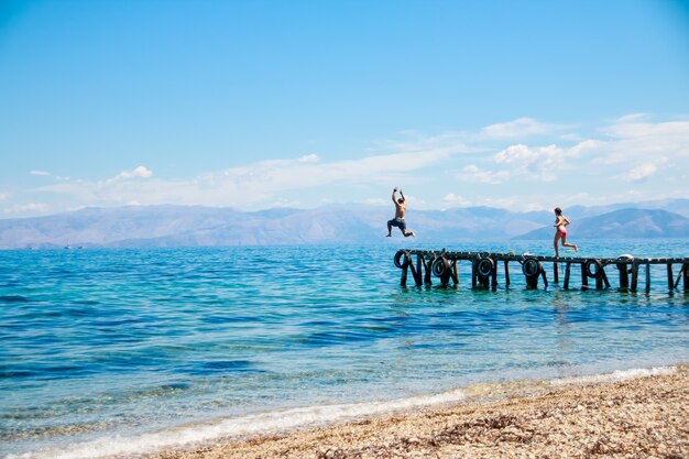 Adolescenti che salta giù dal molo in mare.