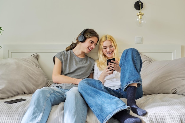 Adolescenti hipster che ridono felici maschi e femmine divertendosi utilizzando lo smartphone insieme