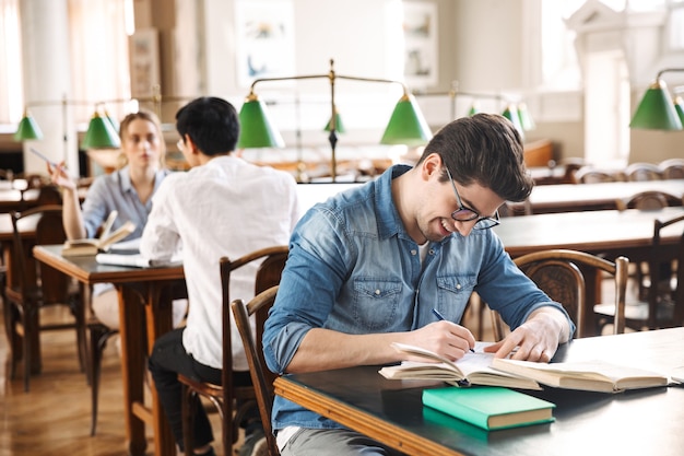 Adolescenti intelligenti e allegri che studiano insieme in biblioteca, leggendo libri