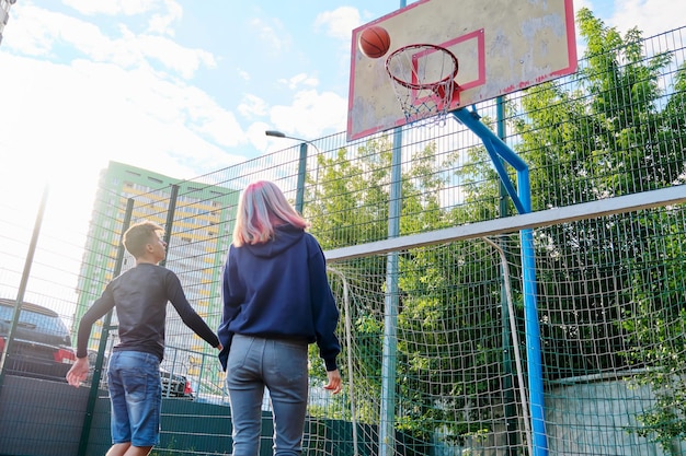 Adolescenti ragazzo e ragazza su un campo da basket all'aperto giocando a basket di strada