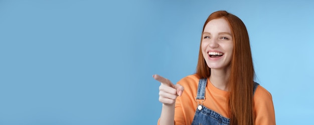 Adorabile affascinata giovane attraente tenera rossa divertita ragazza che si diverte indicando a sinistra