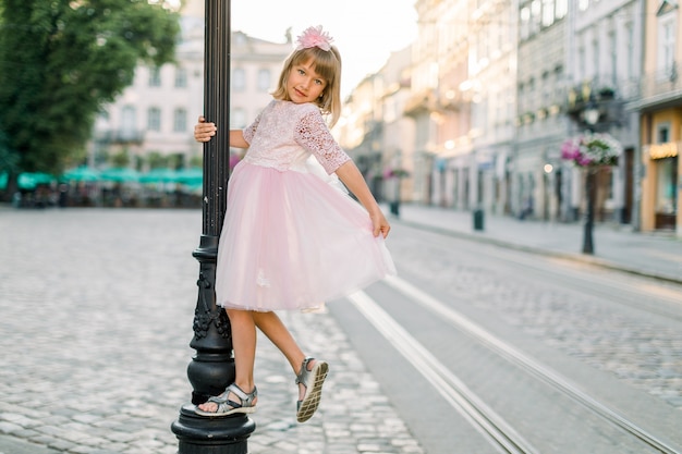 Adorabile bambina bionda in un abito rosa in città