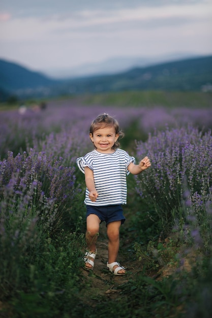 Adorabile bambina che cammina nel campo di lavanda dopo il tramonto Lavanda blu o viola Bambino felice sorriso correre e saltare