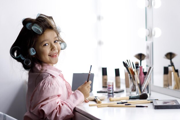 Adorabile bambina che gioca con il cosmetico di sua madre davanti allo specchio a casa