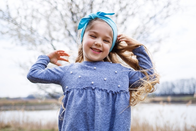 Adorabile bambina che gioca nel giardino di melo in fiore durante la caccia alle uova di Pasqua, correndo e sorridendo. Bambino nel frutteto primaverile con fiori di ciliegio.