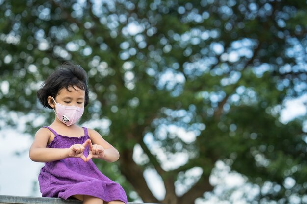 Adorabile bambina che indossa una maschera protettiva seduta contro l'albero della pioggia