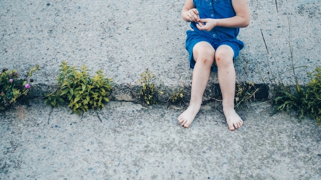 Adorabile bambina che ride sulla natura - ragazza felice in un vestito blu e picchiata per le ginocchia si siede sulle scale. Infanzia felice.