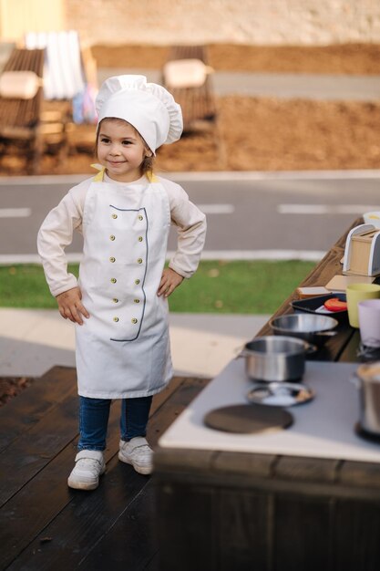 Adorabile bambina con cappotto e cappuccio da chef cuochi nella cucina giocattolo per bambini che giocano sui bambini piccoli