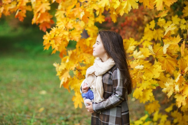 Adorabile bambina con foglie di autunno nel parco di bellezza