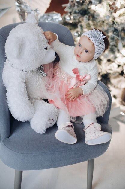 Adorabile bambina con orsacchiotto sulla poltrona vicino all'albero di Natale.