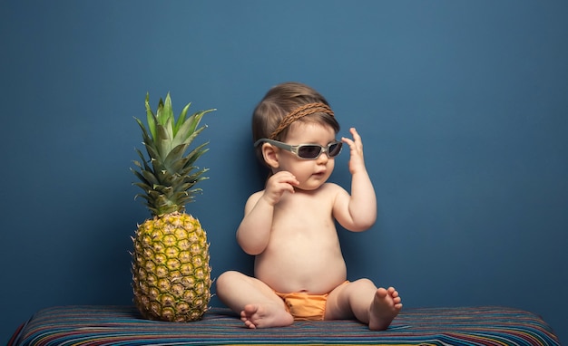 Adorabile bambina felice seduta a giocare con un ananas su sfondo blu