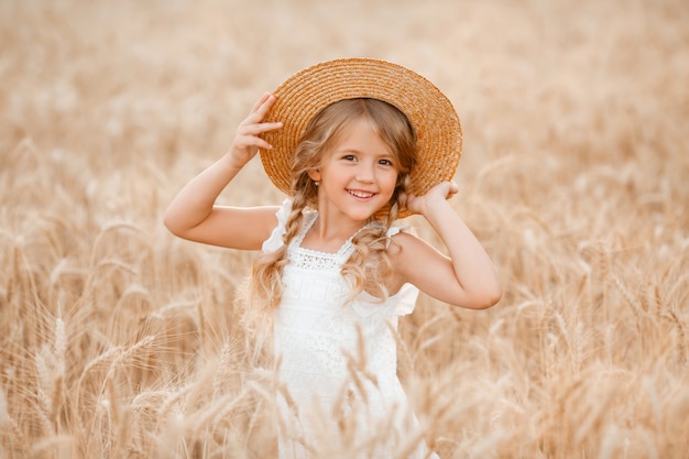 Adorabile bambina gioca su un campo di grano in una calda giornata estiva