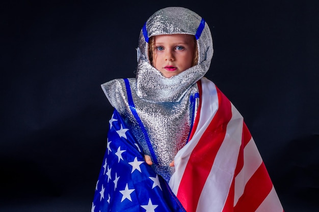 Adorabile bambina in costume casco che gioca brillante lamina d'argento cosmonauta in uniforme con bandiera americana sfondo nero nello studiopatriottismo 20 luglio 1969 sbarco sulla luna concetto spazio giorno