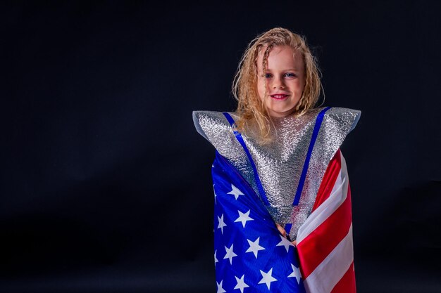 Adorabile bambina in costume casco che gioca brillante lamina d'argento cosmonauta in uniforme con bandiera americana sfondo nero nello studiopatriottismo 20 luglio 1969 sbarco sulla luna concetto spazio giorno