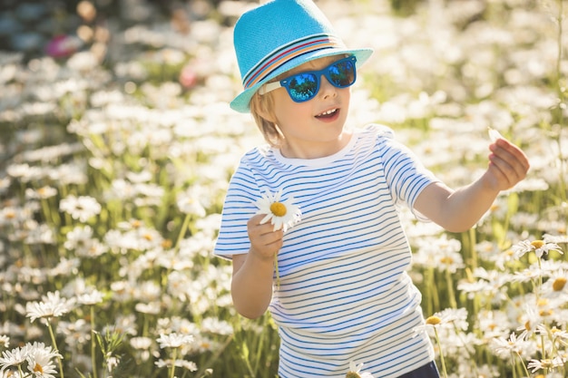 Adorabile bambina nel campo di camomilla che suona mi ama, non mi ama. Ragazzo abbastanza allegro all'aperto con i fiori che strappano un petalo