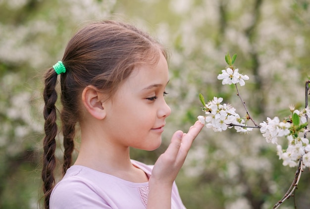 Adorabile bambina nel giardino di ciliegi in fiore in una bella giornata primaverile