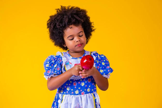 Adorabile bambina nera vestita con abiti da festa di giugno che mangiano Love Apple Apple dessert ricoperto di caramello rosso