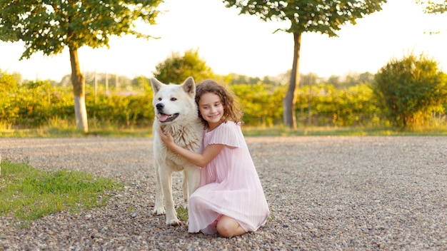 Adorabile bambina riccia Una bambina di 7 anni in abito rosa abbraccia il suo cane preferito durante una passeggiata estiva