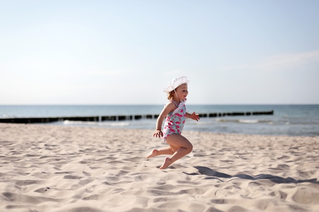 Adorabile bambina sorridente felice in vacanza al mare, saltando in spiaggia