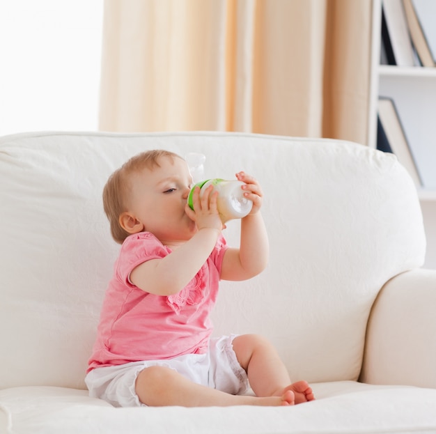 Adorabile bambino biondo biberon mentre seduto su un divano