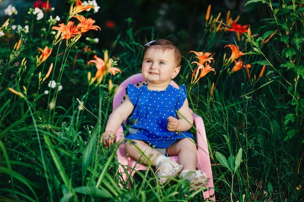 Adorabile bambino carino con vestito blu sorridente in giardino pieno di bellissimi fiori