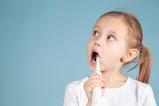 Adorabile bambino caucasico che lava i denti in piedi su sfondo blu, concetto di igiene