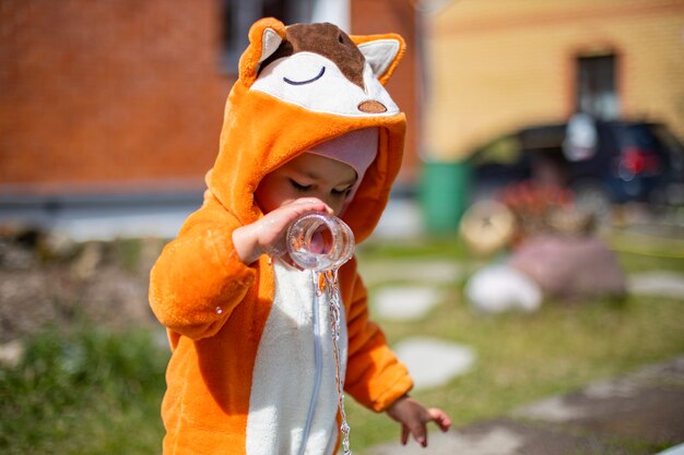 adorabile bambino che gioca con l'acqua nel cortile di casa sotto il sole. bambino in costume da volpe