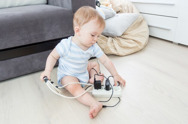 Adorabile bambino che gioca con prolunghe elettriche e fili sul pavimento