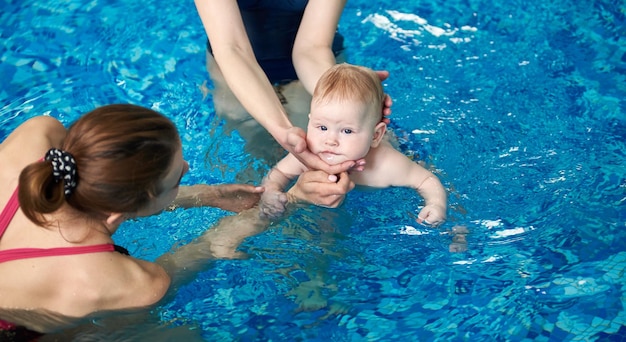 Adorabile bambino che si diverte a nuotare nella piscina per bambini con sua madre e istruttore Istruttore di nuoto per bambini in azione