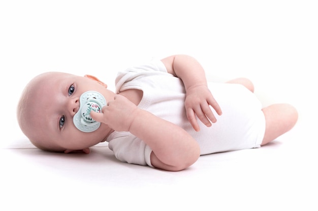 Adorabile bambino con un ciuccio in bocca giace sulla schiena su uno sfondo bianco