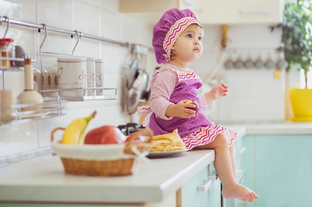 Adorabile bambino in grembiule e berretto da chef seduto con una mela sul tavolo