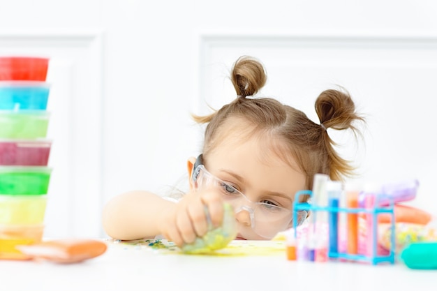 Adorabile bambino in occhiali protettivi studiando chimica facendo soffice melma da ingredienti multicolori in aula