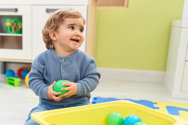 Adorabile bambino ispanico che gioca con le palle seduto sul pavimento all'asilo