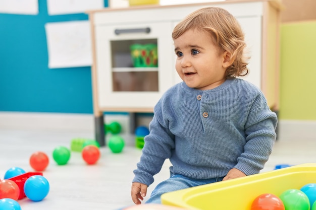 Adorabile bambino ispanico che gioca con le palle seduto sul pavimento all'asilo