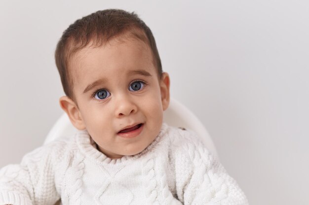 Adorabile bambino ispanico sorridente fiducioso seduto sul seggiolone su sfondo bianco isolato