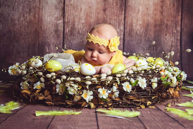 Adorabile bambino sdraiato in un nido gigante decorato con uova di Pasqua e piume di Pasqua