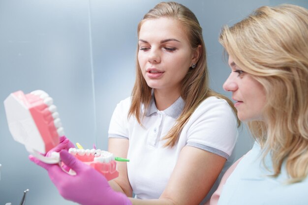 Adorabile dentista che educa la sua paziente matura sull'uso degli spazzolini interdentali