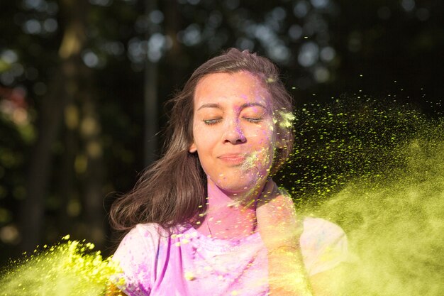 Adorabile donna asiatica bruna in maglietta bianca che si diverte con la polvere gialla di Holi