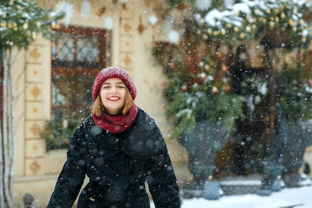 Adorabile donna bruna che indossa berretto rosso e sciarpa godendo nevicata. Spazio vuoto