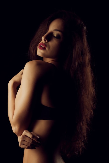 Adorabile donna bruna con un corpo perfetto in posa in lingerie nera al buio