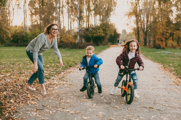 Adorabile fratellino che gareggia con sua sorella in bicicletta all'aperto nel parco mentre la madre gli dà inizio.