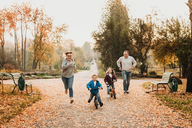 Adorabile fratellino e sorella che vanno in bicicletta mentre i loro genitori li inseguono ridendo all'aperto nel parco.