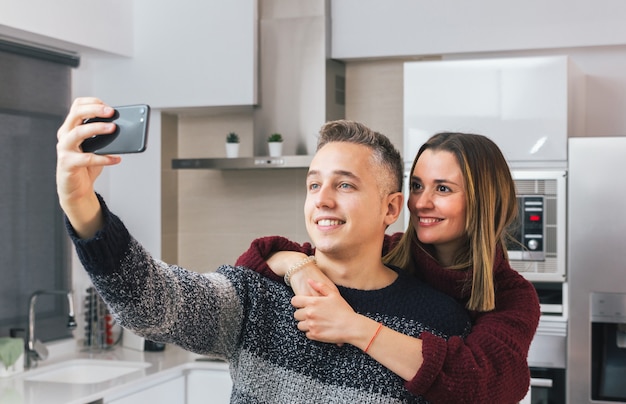 Adorabile giovane coppia sorridente e prendendo un selfie con il cellulare a casa