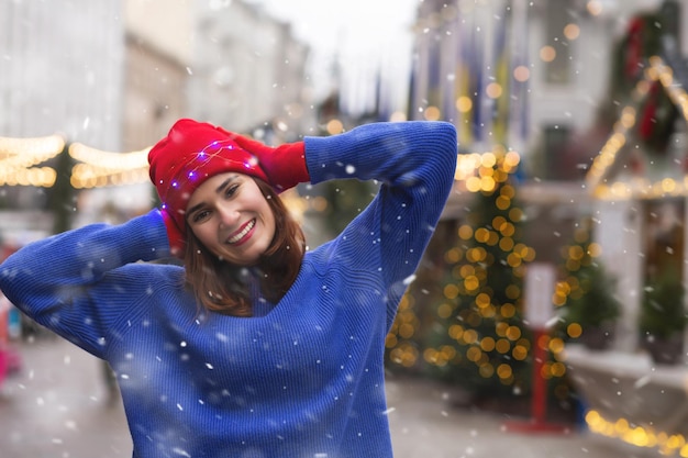 Adorabile giovane donna che trascorre le vacanze invernali alla fiera di Natale durante la nevicata. Spazio per il testo