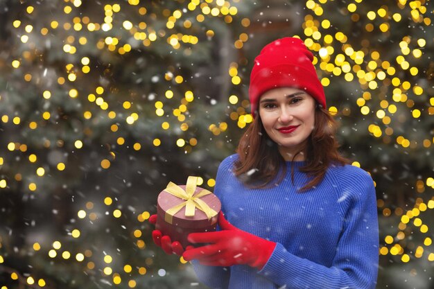 Adorabile giovane donna con scatola regalo con un nastro alla fiera di Natale. Spazio vuoto