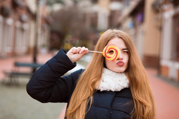 Adorabile giovane donna dai capelli rossi che tiene caramelle colorate di Natale per la strada