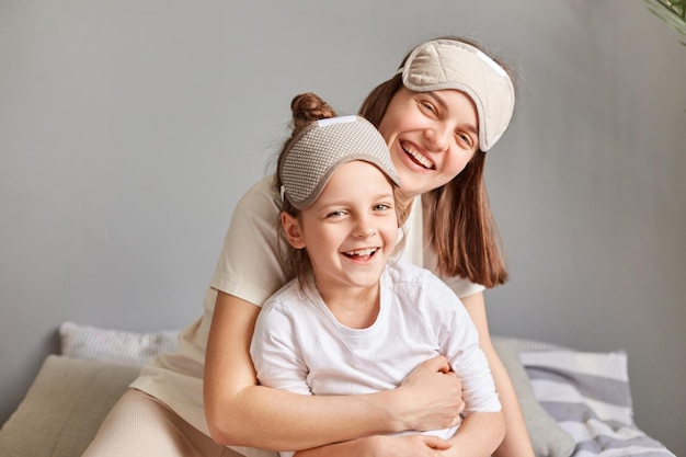 Adorabile madre felice e figlia con gli occhi bendati seduti sul letto in camera da letto che si abbracciano trascorrendo la mattinata insieme sorridendo con felice espressione facciale