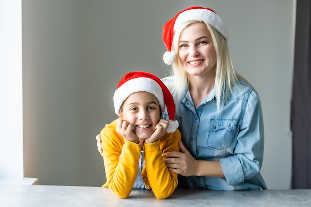 Adorabile mamma bionda caucasica con la figlia che indossano entrambi i cappelli di Babbo Natale