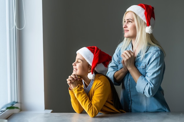 Adorabile mamma bionda caucasica con la figlia che indossano entrambi i cappelli di Babbo Natale