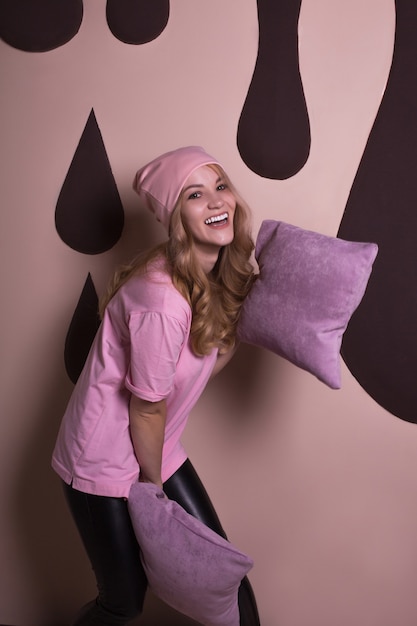 Adorabile modella bionda felice che gioca con i cuscini su uno sfondo rosa per studio